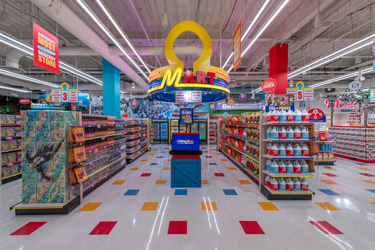 How Omega Mart looks when you first enter it - rows of supermarket shelves with a Ω-shaped display in the center. The main color scheme is white, yellow, red, and light blue.